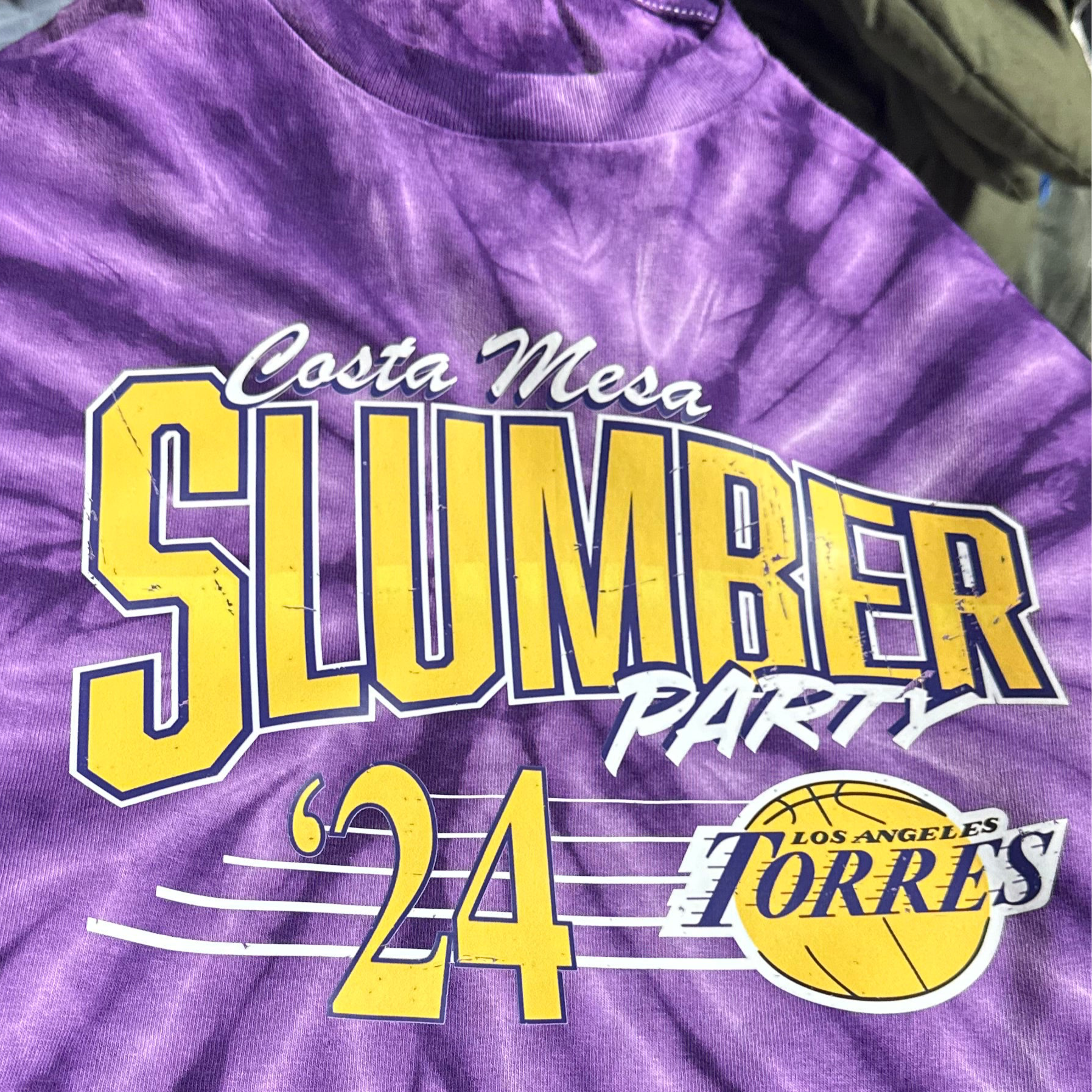 Purple tie-dye t-shirt with yellow text and a logo, hanging on a rack.